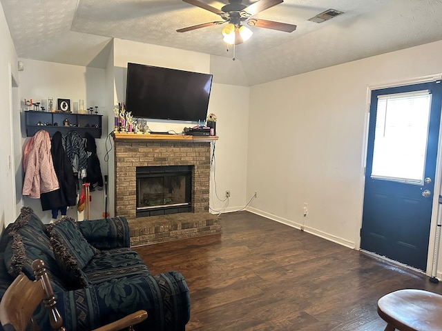 living room featuring ceiling fan, dark hardwood / wood-style flooring, a textured ceiling, and a brick fireplace