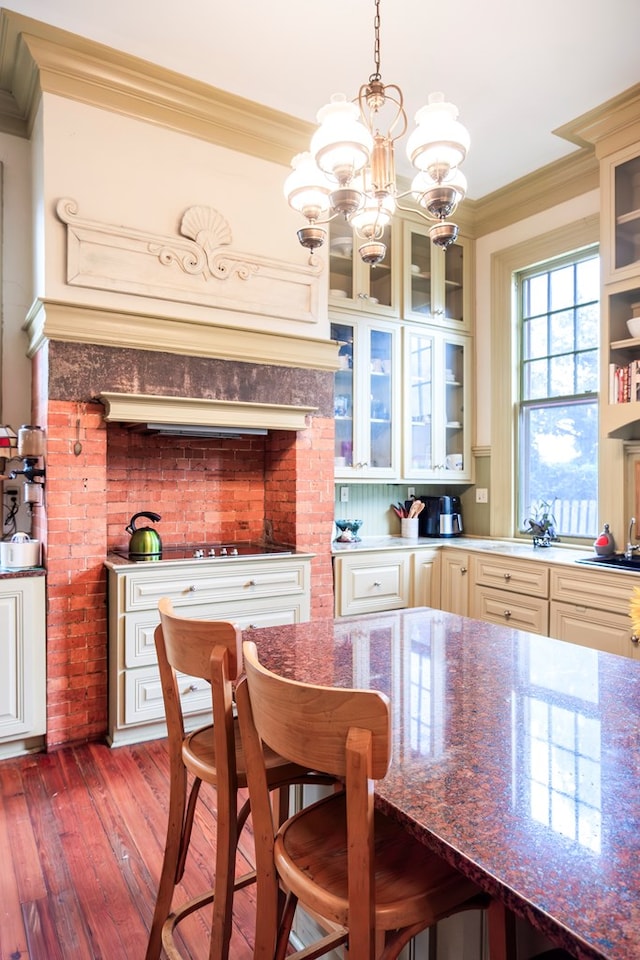 kitchen featuring hanging light fixtures, an inviting chandelier, crown molding, dark stone counters, and wood-type flooring