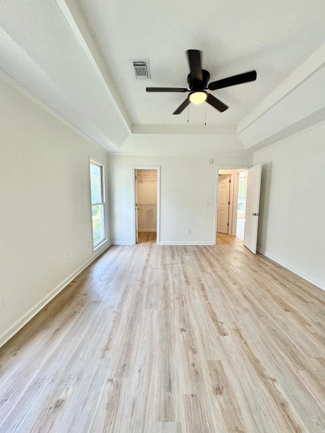 unfurnished bedroom featuring visible vents, baseboards, light wood-type flooring, a raised ceiling, and a spacious closet