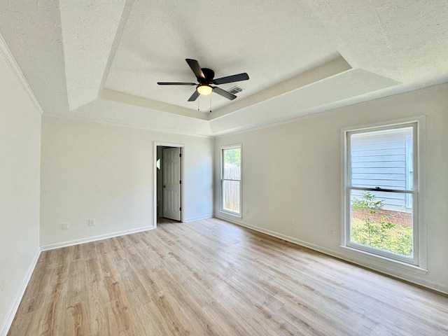 empty room featuring a ceiling fan, a textured ceiling, light wood finished floors, and a raised ceiling