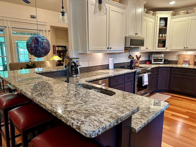 kitchen featuring appliances with stainless steel finishes, a breakfast bar, a peninsula, and light stone counters