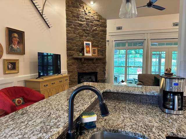 living area featuring ceiling fan, lofted ceiling, a stone fireplace, and visible vents