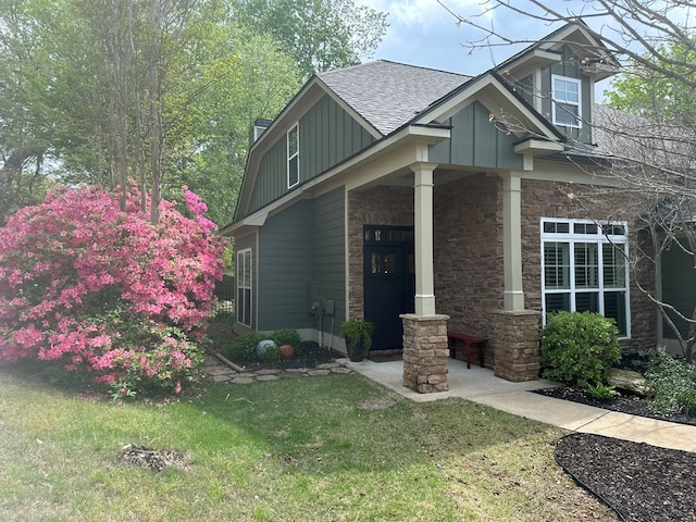 view of front facade featuring covered porch, a front yard, stone siding, roof with shingles, and board and batten siding