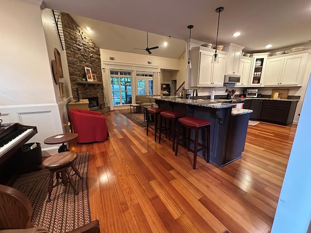 kitchen featuring a breakfast bar area, stone countertops, stainless steel microwave, glass insert cabinets, and white cabinetry