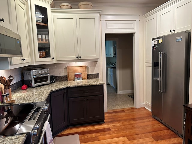 kitchen featuring light wood-style floors, appliances with stainless steel finishes, tasteful backsplash, and glass insert cabinets