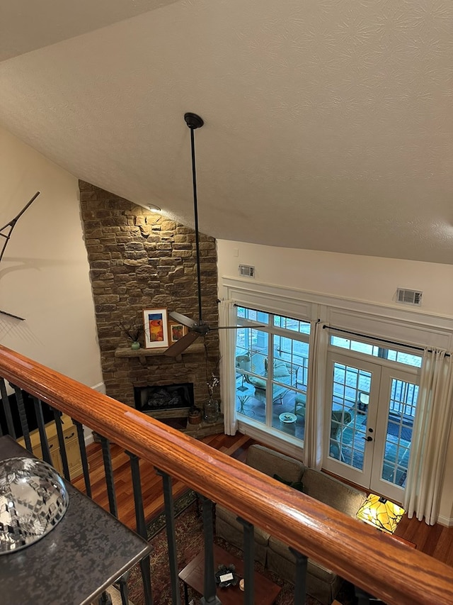 staircase featuring a stone fireplace, french doors, wood finished floors, vaulted ceiling, and visible vents
