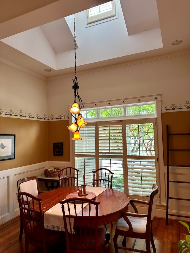 dining space featuring a tray ceiling, ornamental molding, wood finished floors, and a wainscoted wall