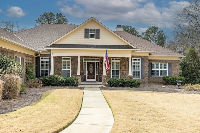 craftsman inspired home with stone siding, a shingled roof, a chimney, and brick siding