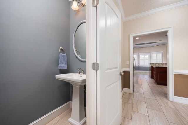 bathroom featuring a sink, crown molding, a textured ceiling, and baseboards