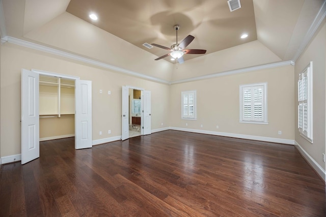 unfurnished bedroom featuring a tray ceiling, visible vents, baseboards, and wood finished floors