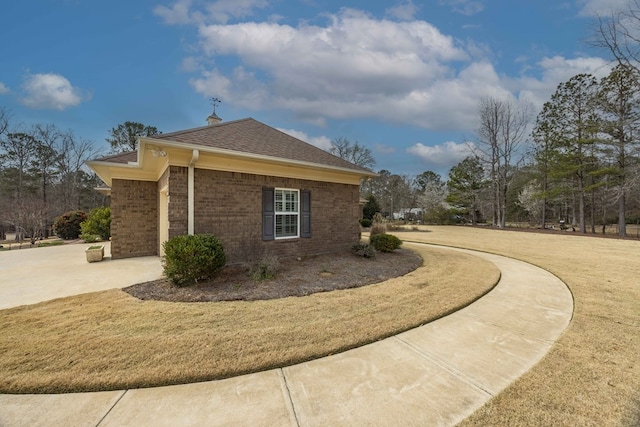 view of side of property with roof with shingles, brick siding, and a lawn