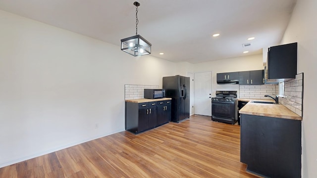 kitchen featuring backsplash, under cabinet range hood, light wood-type flooring, black appliances, and a sink