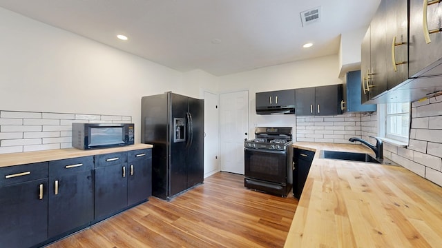 kitchen featuring under cabinet range hood, butcher block countertops, black appliances, and a sink