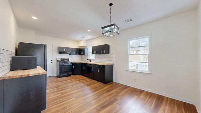 kitchen with range with gas stovetop, dark cabinets, a sink, light wood-type flooring, and butcher block counters