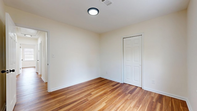 unfurnished room with light wood finished floors, visible vents, attic access, and baseboards