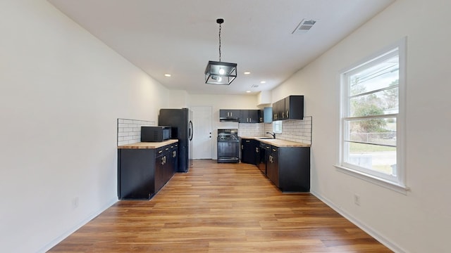 kitchen featuring tasteful backsplash, light wood finished floors, pendant lighting, black appliances, and a sink