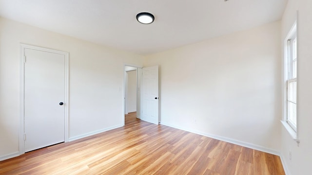 unfurnished bedroom featuring multiple windows, baseboards, and light wood finished floors