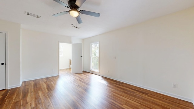 empty room with ceiling fan, visible vents, baseboards, and wood finished floors