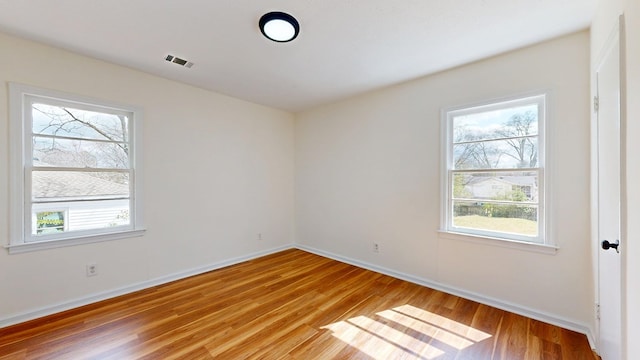 empty room with light wood-style floors, visible vents, and baseboards