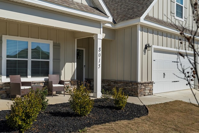 doorway to property with roof with shingles, covered porch, board and batten siding, a garage, and stone siding