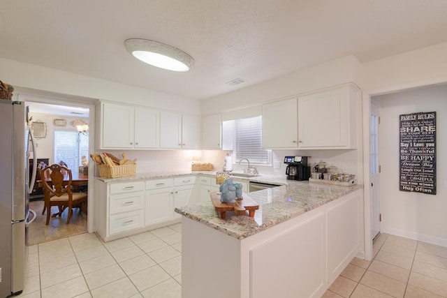 kitchen featuring light tile patterned floors, a peninsula, a sink, and freestanding refrigerator