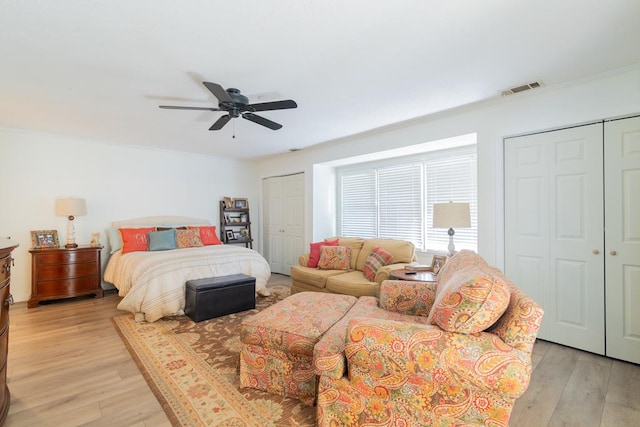 bedroom featuring light wood-type flooring, multiple closets, visible vents, and ceiling fan