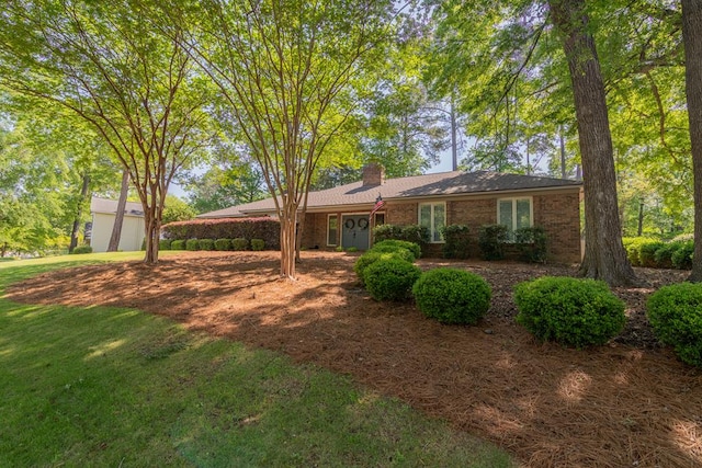 single story home featuring brick siding, a chimney, and a front yard