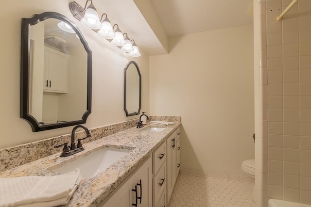 bathroom with double vanity, tile patterned floors, toilet, and a sink