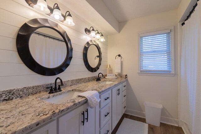 full bath featuring baseboards, wood finished floors, a sink, and double vanity