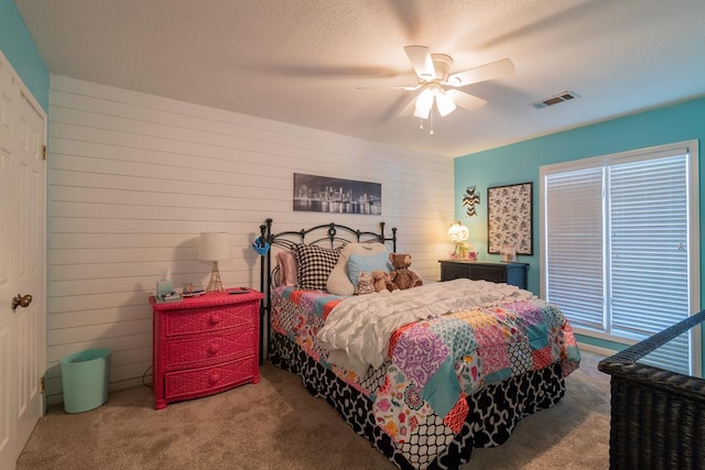 bedroom with wooden walls, visible vents, a textured ceiling, carpet flooring, and ceiling fan