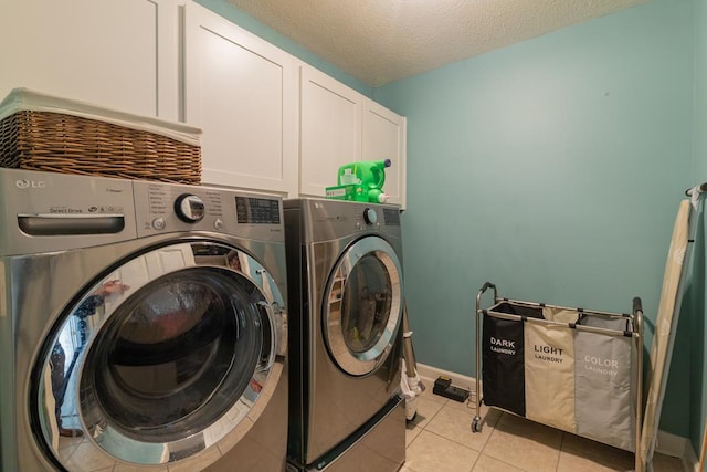 laundry area featuring washing machine and clothes dryer, a textured ceiling, light tile patterned flooring, baseboards, and cabinet space