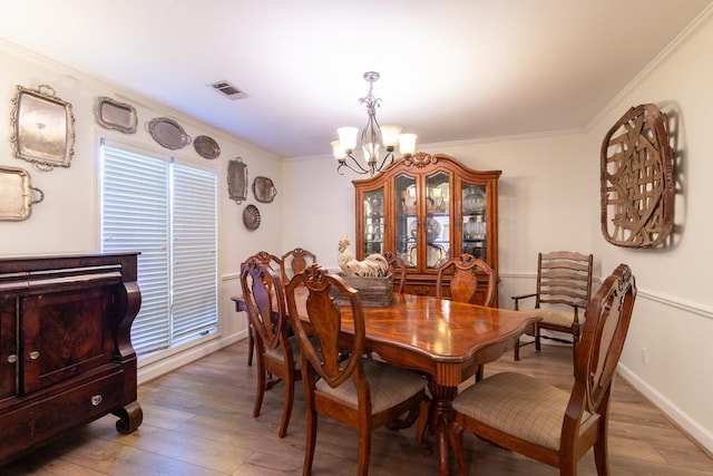 dining area with light wood-style floors, an inviting chandelier, baseboards, ornamental molding, and visible vents