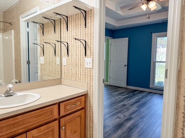 full bath with a ceiling fan, wood finished floors, wallpapered walls, baseboards, and vanity