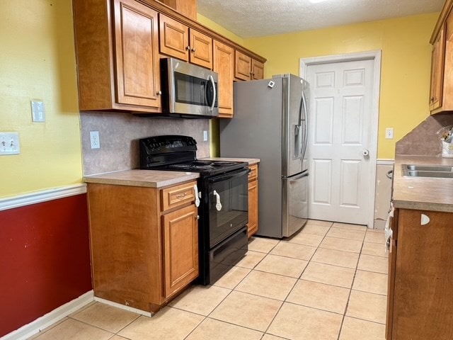 kitchen with light tile patterned floors, appliances with stainless steel finishes, brown cabinetry, and a sink