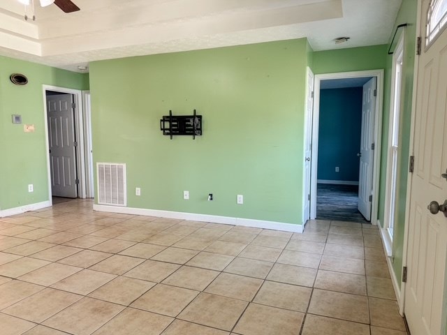 empty room featuring light tile patterned floors, a ceiling fan, visible vents, and baseboards