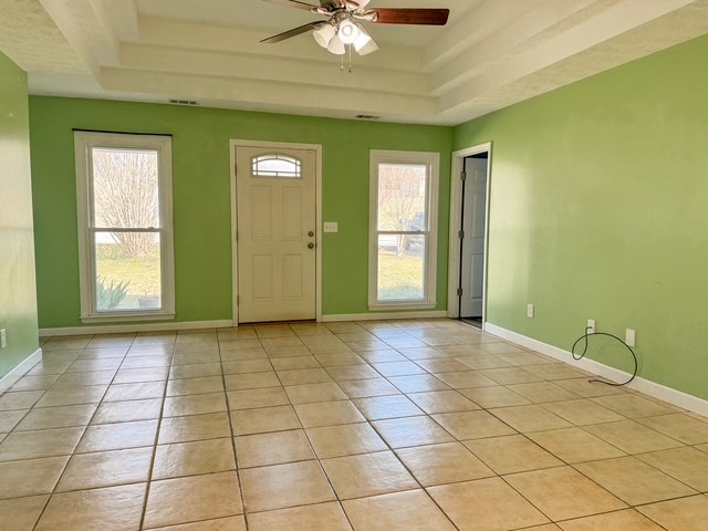 entrance foyer with visible vents, baseboards, a tray ceiling, light tile patterned floors, and a ceiling fan