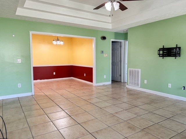 empty room with light tile patterned floors, visible vents, a raised ceiling, and baseboards