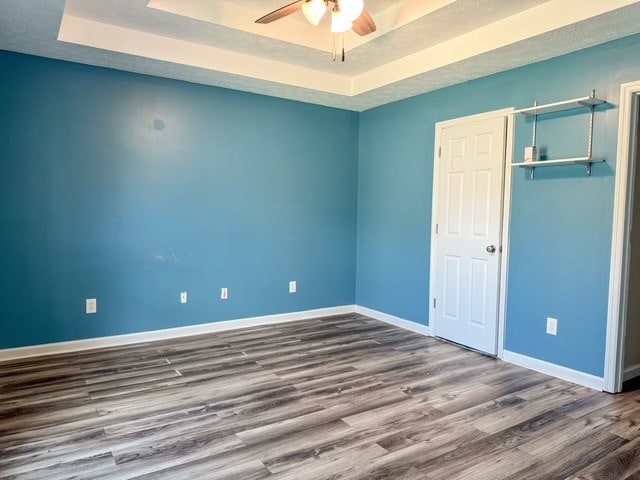 unfurnished bedroom with ceiling fan, baseboards, wood finished floors, a closet, and a raised ceiling