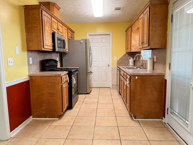 kitchen featuring black gas range oven, visible vents, light tile patterned flooring, a sink, and stainless steel microwave