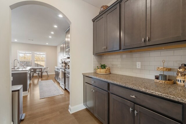 kitchen featuring stainless steel appliances, light stone counters, tasteful backsplash, hanging light fixtures, and a kitchen island with sink