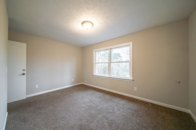 spare room featuring a textured ceiling and dark carpet