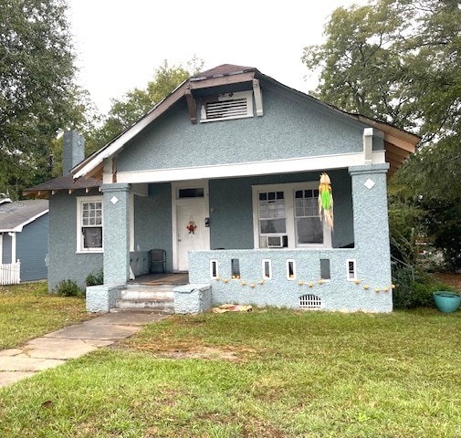 bungalow-style home featuring covered porch, a front lawn, and stucco siding