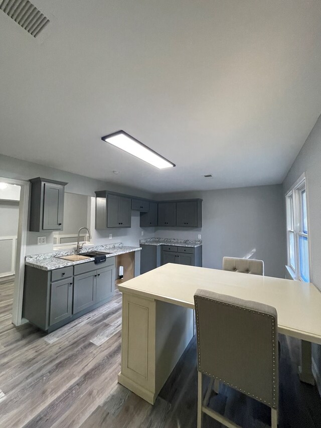 kitchen with sink, gray cabinets, a kitchen island, a kitchen bar, and wood-type flooring