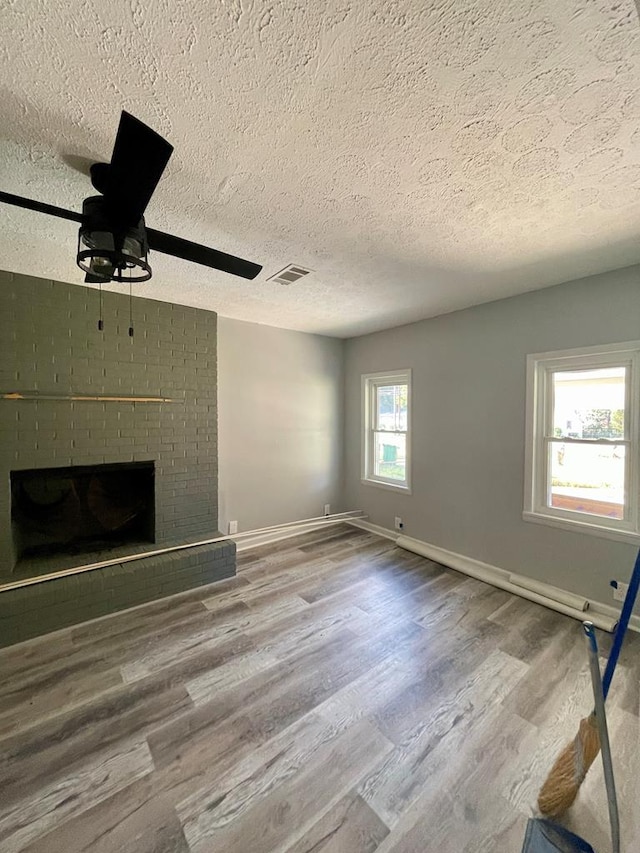 unfurnished living room featuring a fireplace, a textured ceiling, hardwood / wood-style flooring, and ceiling fan