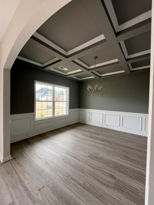 unfurnished room with visible vents, a chandelier, wainscoting, wood finished floors, and arched walkways