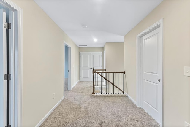 hall with an upstairs landing, carpet flooring, visible vents, and baseboards