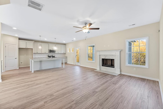 unfurnished living room with plenty of natural light, a ceiling fan, and visible vents