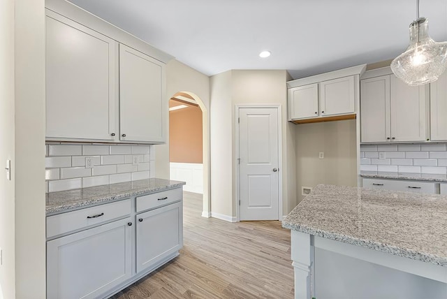 kitchen with light stone counters, tasteful backsplash, arched walkways, light wood finished floors, and hanging light fixtures