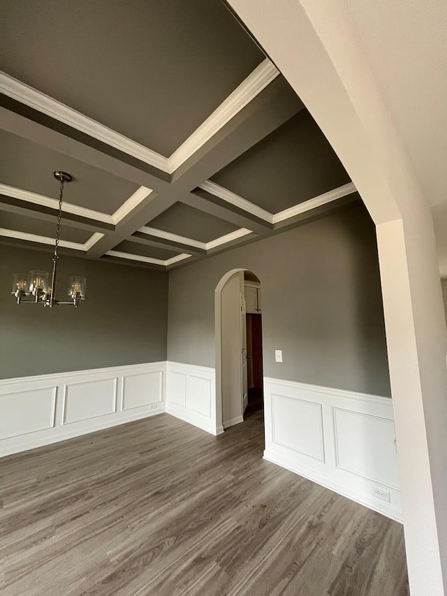 empty room with arched walkways, a chandelier, dark wood finished floors, and coffered ceiling