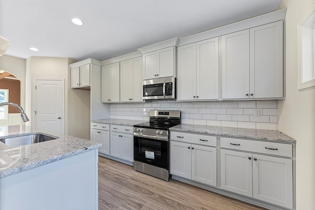 kitchen with light wood-style flooring, arched walkways, a sink, appliances with stainless steel finishes, and tasteful backsplash